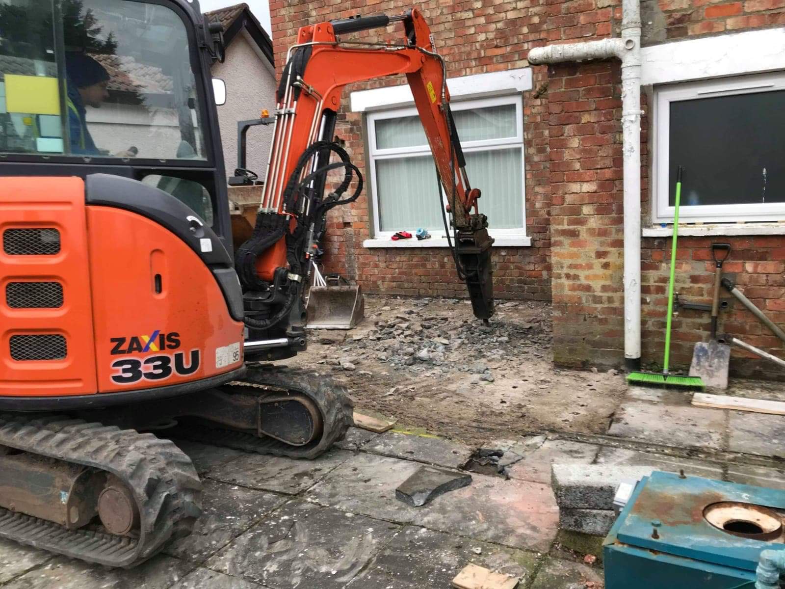 A mini-excavator with a breaker attachment lifting an old patio.