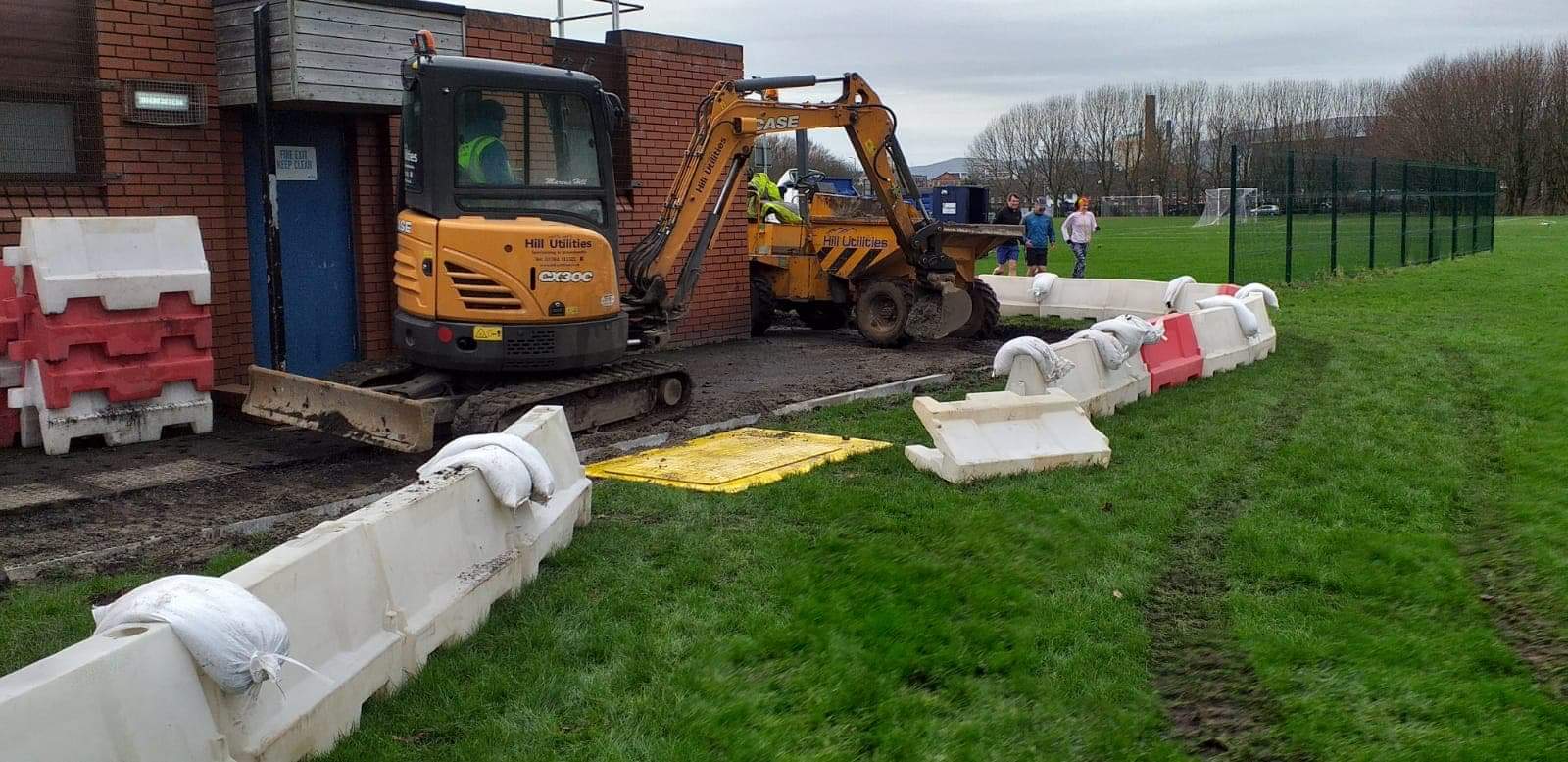 Groundworks alongside a sports pavilion, with site safety barriers in place.