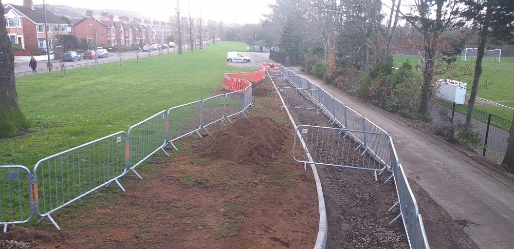 A fenced drainage trench excavated along a parkland path.