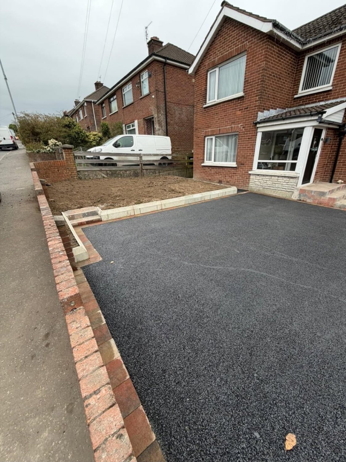 A finished tarmac driveway, edged with brick paviours.