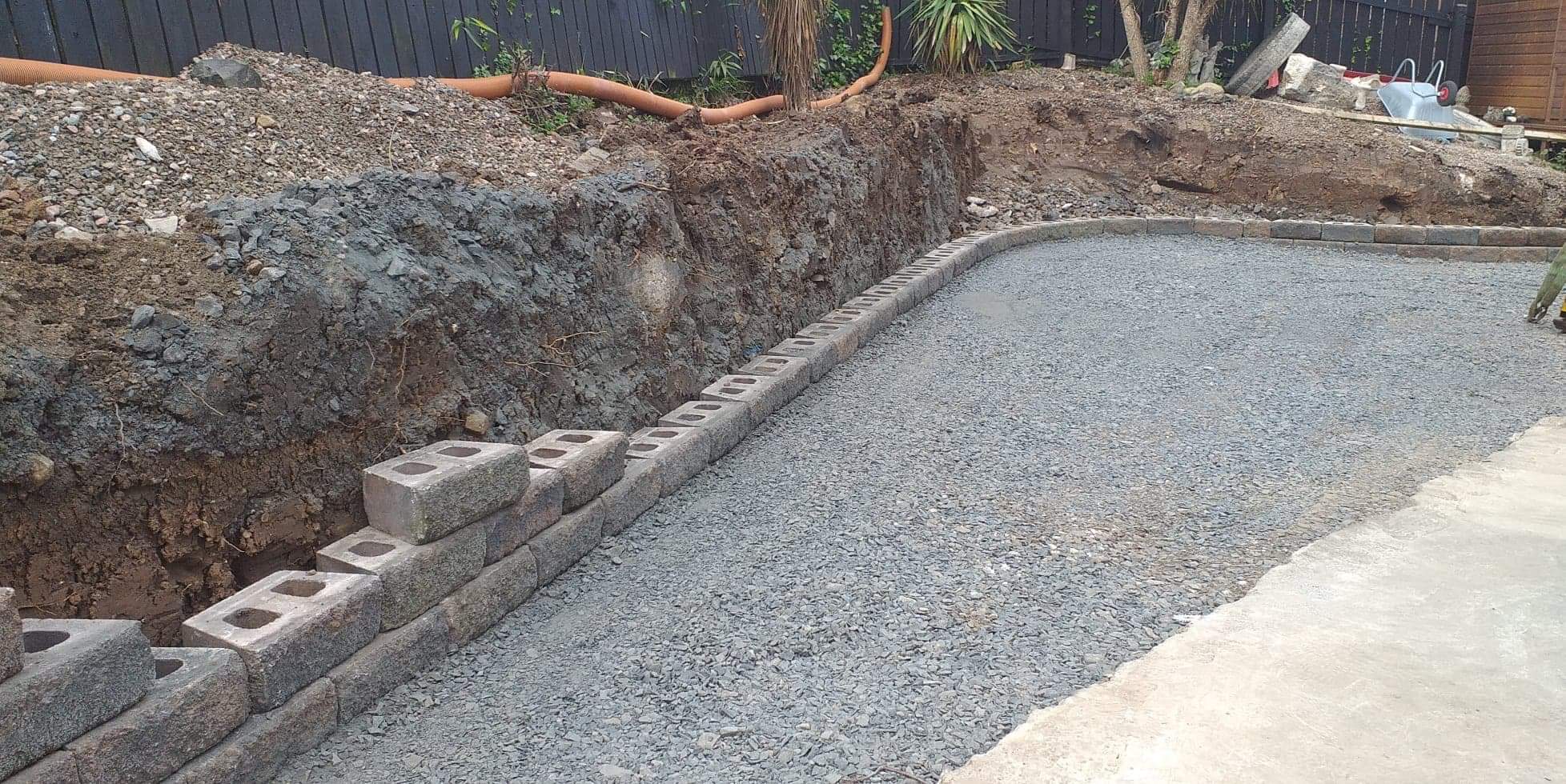 A retaining wall and driveway sub-base under construction in a sloped garden.
