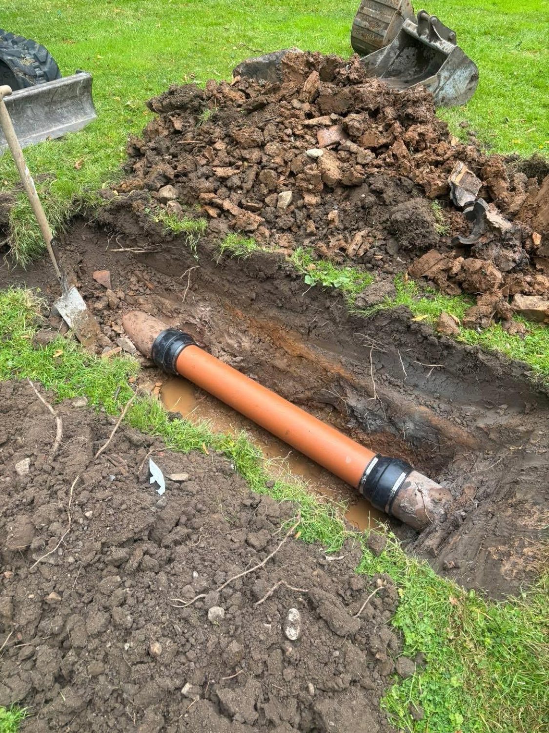 Replacing a section of underground drainage pipe in a garden lawn.