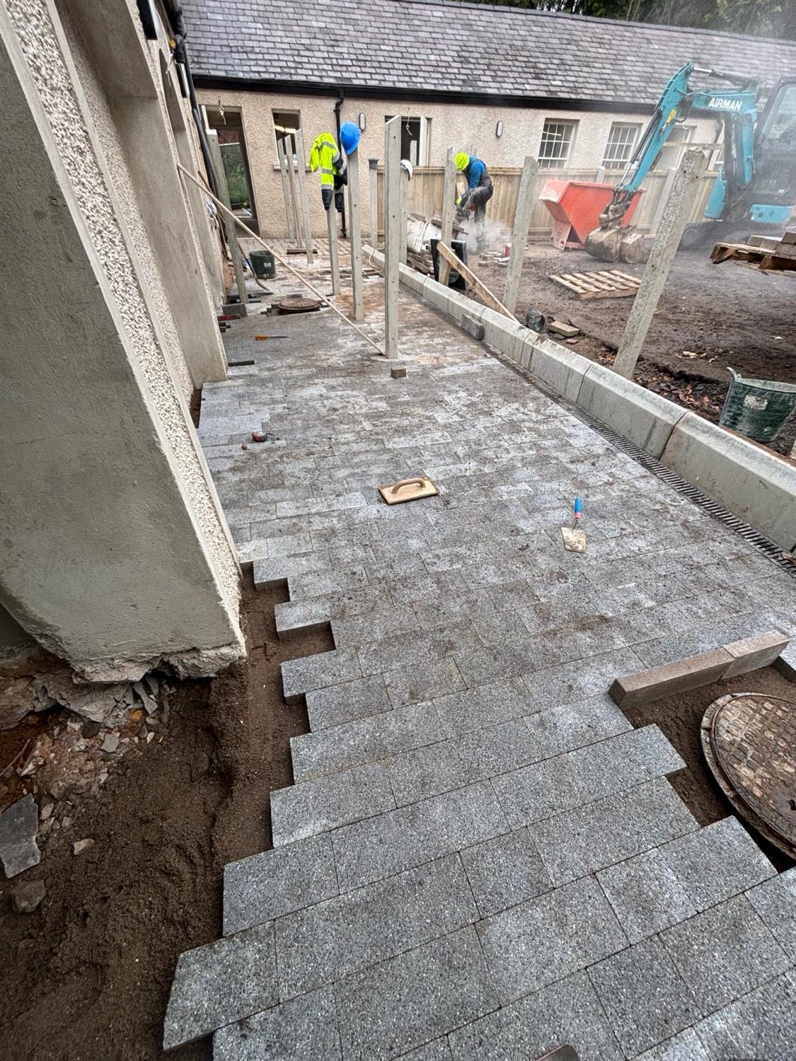 A new granite-paved path and fence line being built in a courtyard.