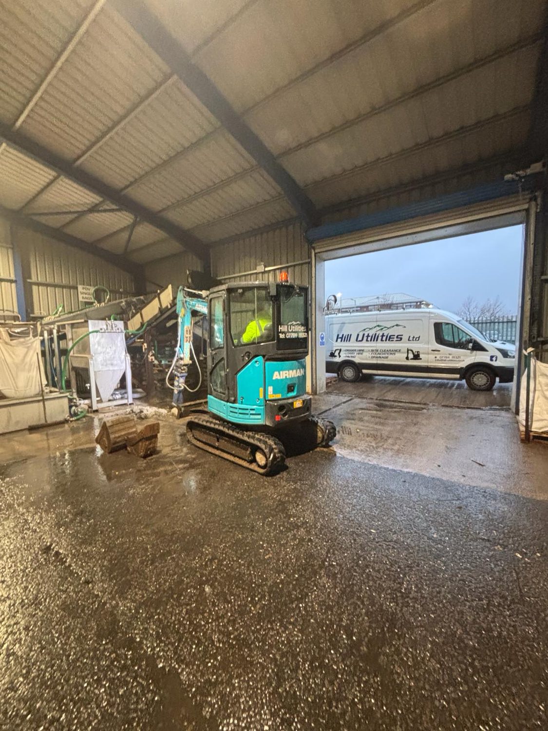A tracked mini-excavator and Hill Utilities van at the company yard.